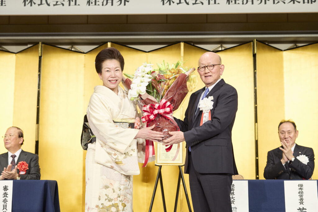 審査委員長の武藤敏郎 大和総研名誉理事から表彰状を、弊社社長の佐藤有美から花束を受け取る岡藤会長CEO