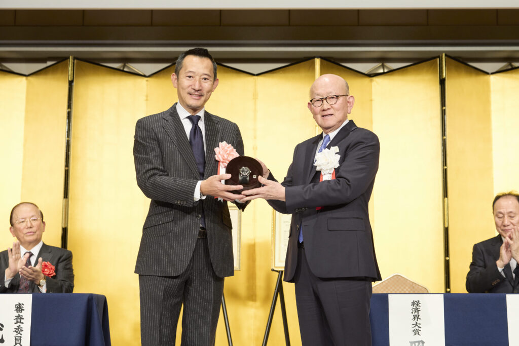 岡藤会長CEOには副賞として、麦野豪　オフィス麦野代表より高級腕時計「トラベルセトロ」が贈られた